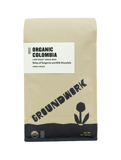 A brown bag of Groundwork Coffees Colombia: AMUCC Fair Trade whole bean coffee with tangerine and milk chocolate notes, simple flower graphic, and USDA Organic seal.