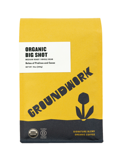 A yellow and black bag of Groundwork Coffee Big Shot Medium Roast whole bean coffee with certification logos, a tulip graphic, and notes of praline and cacao.